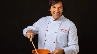 Valerio Merola in tenuta da chef mentre prepara una ricetta in cucina.