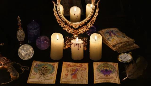 Specchio dorato, candele accese e carte su un tavolo scuro