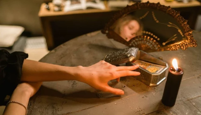 Mano accanto a carte, specchio e candela nera